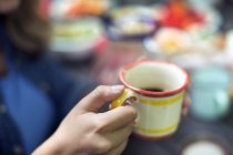 Close-up of mug with coffee in female hand at table. — Stock Photo