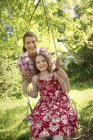 Mature woman and girl in sundress on swing in garden. — Stock Photo