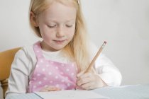 Blondes Mädchen im Grundalter sitzt am Tisch und zeichnet mit Bleistift. — Stockfoto