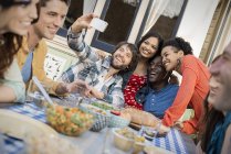 Group of men and women gathering around table and taking selfie. — Stock Photo