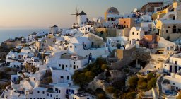 Windmill in cityscape of hilltop town of whitewashed houses at sunset, Santorini, Greece. — Stock Photo