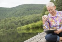 Frau sitzt draußen auf Steg und nutzt digitales Tablet. — Stockfoto