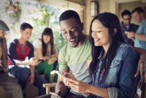 Man and woman holding smartphones with fiends at house party. — Stock Photo