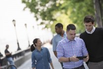 Cuatro personas caminando en la calle y hombre adulto medio usando tableta digital . - foto de stock