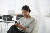 Весела бізнес-леді використовує смартфон у зручному кріслі в офісі . — стокове фото