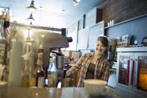 Female barista behind coffee machine at coffee shop with cappuccino in white cup on counter. — Stock Photo