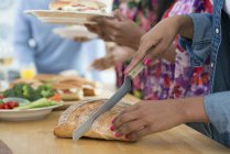 Vista cortada de mãos femininas cortando pão na mesa do buffet na festa . — Fotografia de Stock