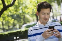 Молодой человек проверяет смартфон, сидя в городском парке
. — стоковое фото