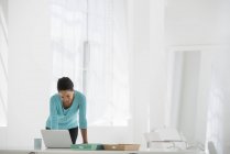 Femme penchée sur le bureau et utilisant un ordinateur portable au bureau . — Photo de stock