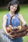 Woman standing in garden and holding basket of vegetables. — Stock Photo