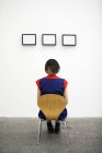 Rückansicht einer Frau, die auf einem Stuhl sitzt und sich Kunstwerke in der Galerie ansieht. — Stockfoto
