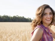 Mujer joven de pie en el campo de maíz, sonriendo y mirando a la cámara
. - foto de stock