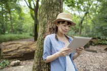 Молода жінка використовує цифровий планшет у сонячному лісі . — стокове фото