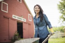 Junge Frau schiebt Karren bei traditionellem Bauernhof auf dem Land — Stockfoto
