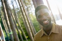 Young man smiling and looking in camera under shade of trees in woods. — Stock Photo