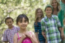 Elementary age girl and group of children and adults posing outdoors in garden. — Stock Photo