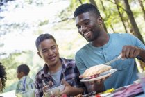Young man and boy cutting fruit pie at picnic table. — Stock Photo