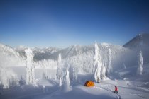Mann zu Fuß zu orangefarbenem Zelt in schneebedeckter Berglandschaft in den USA. — Stockfoto