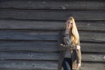 Junge Frau lehnt an Holzscheune und blickt im Winter in die Kamera. — Stockfoto