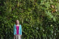 Menina em pé na frente da parede coberta com samambaias e plantas de escalada . — Fotografia de Stock
