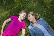 Mutter und Tochter liegen auf grünem Rasen, schauen einander an und lächeln. — Stockfoto