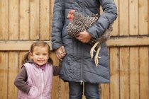 Woman in grey coat holding black and white chicken and holding hands with girl. — Stock Photo