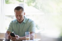 Man with short hair sitting at cafe table and using smartphone. — Stock Photo