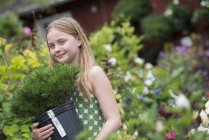 Niña pre-adolescente llevando planta verde en maceta en vivero de plantas orgánicas . - foto de stock