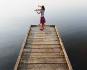 Violinista feminina pré-adolescente tocando violino ao amanhecer no cais de madeira no lago . — Fotografia de Stock