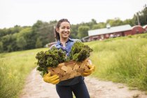 Frau hält Korb mit grünem, frisch gepflücktem Gemüse auf Biohof. — Stockfoto