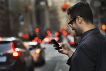 Человек проверяет смартфон на оживленной улице в городе . — стоковое фото