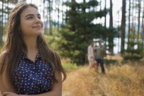 Junge Frau steht im Wald am See mit Menschen im Hintergrund. — Stockfoto