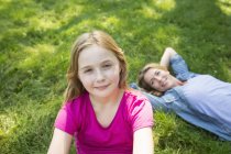 Pre-adolescent girl looking in camera with woman lying on lawn at garden. — Stock Photo