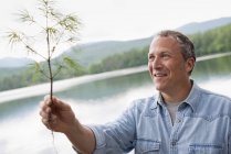 Mature man standing on shore of lake and holding twig. — Stock Photo