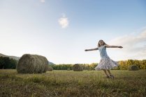 Elementary age girl in dress dancing with arms outstretched on stubble field. — Stock Photo