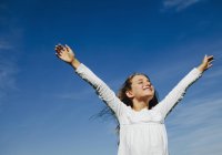 Портрет впевненої дівчини початкового віку з піднятими руками на тлі блакитного неба — стокове фото