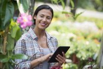Young woman in organic nursery greenhouse using digital tablet. — Stock Photo