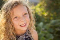 Elementary age girl with curly hair in sunny garden. — Stock Photo
