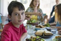Pre-adolescent boy looking in camera with family at dinner table. — Stock Photo