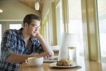 Young man sitting at cafe table and using laptop. — Stock Photo