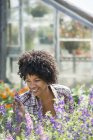 Mulher sorridente cuidando de plantas floridas em viveiro de plantas . — Fotografia de Stock