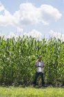 Молодий чоловік у повсякденному одязі стоїть перед посівами кукурудзи і тримає цифровий планшет . — стокове фото