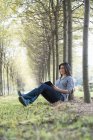 Woman sitting and reading book under trees in woodland. — Stock Photo