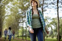 Young woman in a straw hat walking in woods with friends in background. — Stock Photo