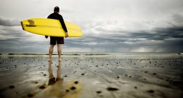 Hombre de mediana edad con tabla de surf de pie en la costa de Rockport Beach en Nueva Inglaterra . - foto de stock