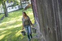 Woman carrying buckets by country barn at farm. — Stock Photo
