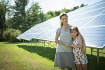 Menina pré-adolescente com mãe posando ao lado de painéis solares na fazenda . — Fotografia de Stock