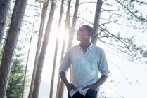 Homem de pé à sombra de pinheiros no verão e olhando para cima . — Fotografia de Stock