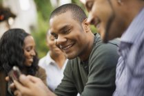 Sorrindo homens olhando para smartphone com mulheres em segundo plano . — Fotografia de Stock