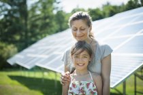 Vorpubertierendes Mädchen posiert mit Mutter neben Solarzellen auf Bauernhof. — Stockfoto